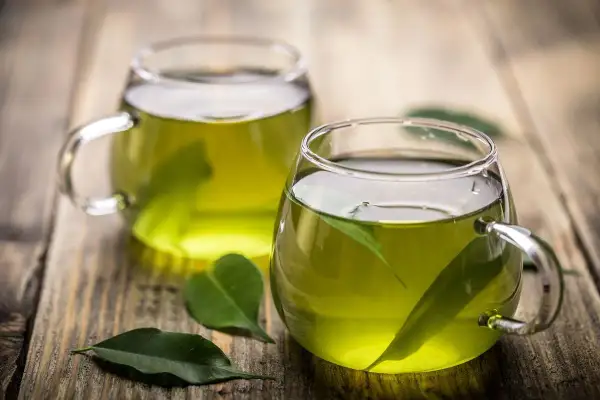 Due tazze di tè verde, con foglie fresche immerse, pronte per gustare le loro proprietà benefiche.