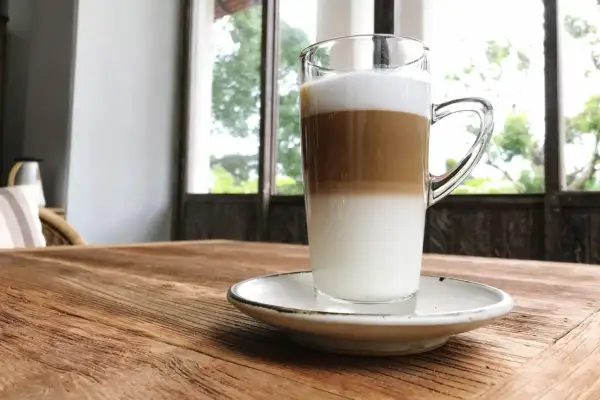 Un macchiatone, un caffè stratificato in un bicchiere trasparente, su un tavolo di legno rustico.