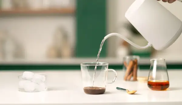 Preparazione di un delizioso spanish latte: acqua calda versata su caffè, cubetti di ghiaccio e un tocco di dolcezza.