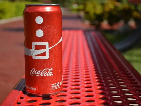 Lattina di Coca-Cola su panchina rossa, con gocce d'acqua. Attenzione, la Coca-Cola fa alzare la pressione!