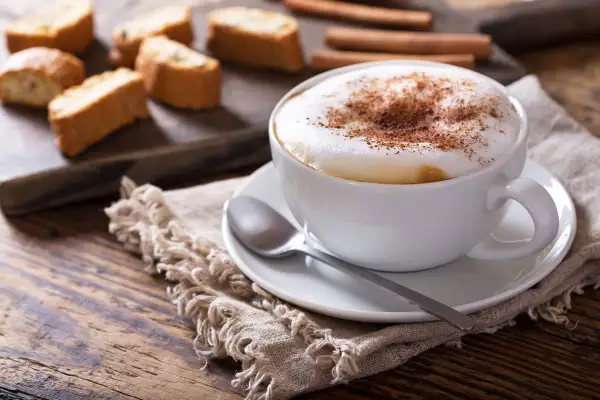 Un cappuccino cremoso con cacao, biscotti e cannella. La schiuma del cappuccino si smonta velocemente se non preparata correttamente.