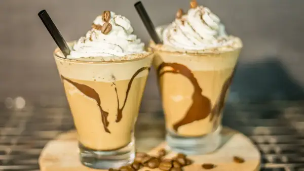 Due deliziosi milkshake al caffè, guarniti con panna montata, chicchi di caffè e sciroppo al cioccolato, pronti per essere gustati.