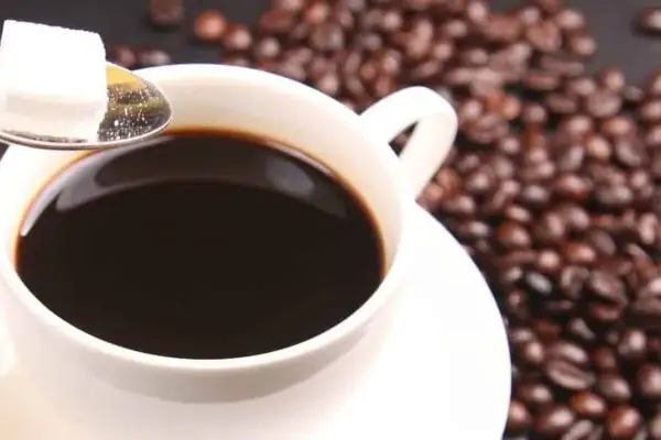 Tazza di caffè decaffeinato, chicchi tostati e zolletta di zucchero su cucchiaino. Ideale per chi vuole godersi il gusto senza preoccuparsi della pressione.