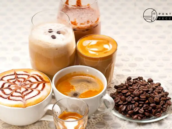 Varietà di deliziosi caffè italiani: un espresso, un cappuccino decorato, un caffè macchiato e un frappé. Chicchi di caffè tostati completano la scena.