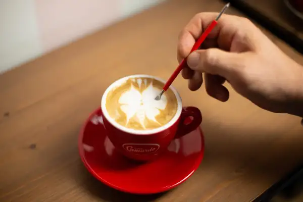 Un barista crea disegni sul cappuccino con uno strumento, mostrando come fare latte art.