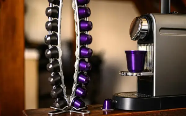 Macchina caffè Caffitaly con spia rossa lampeggiante. Capsule nere e viola in un portacapsule accanto.
