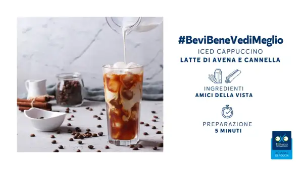 Un rinfrescante cappuccino di avena freddo versato in un bicchiere con ghiaccio, circondato da chicchi di caffè e cannella.
