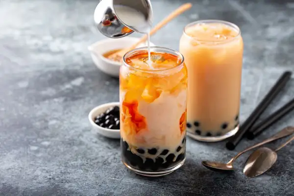 Due bicchieri di bubble tea con perle di tapioca. Un bicchiere è in preparazione con latte versato su un tè arancione.